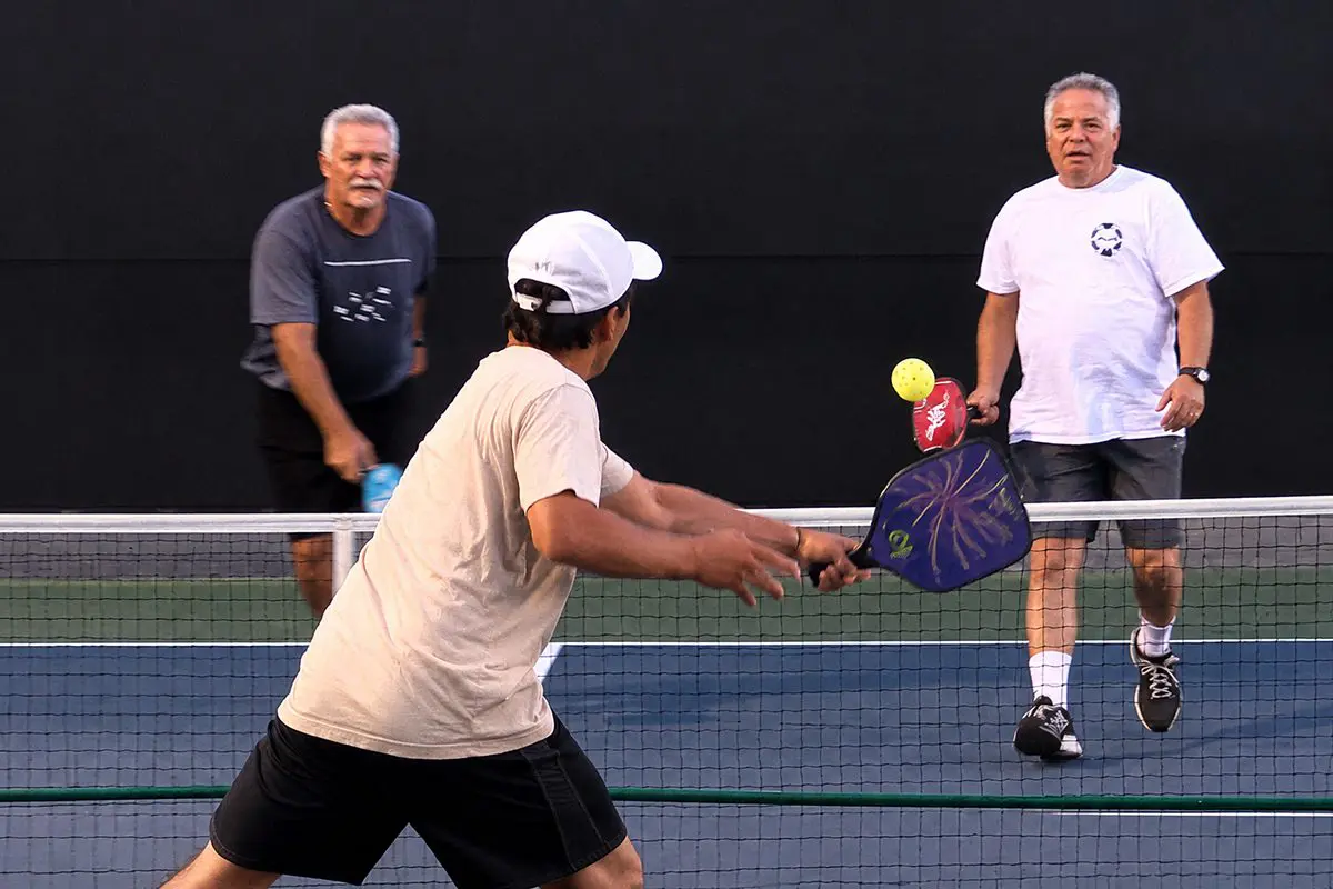 Three men playing pickleball on outdoor court