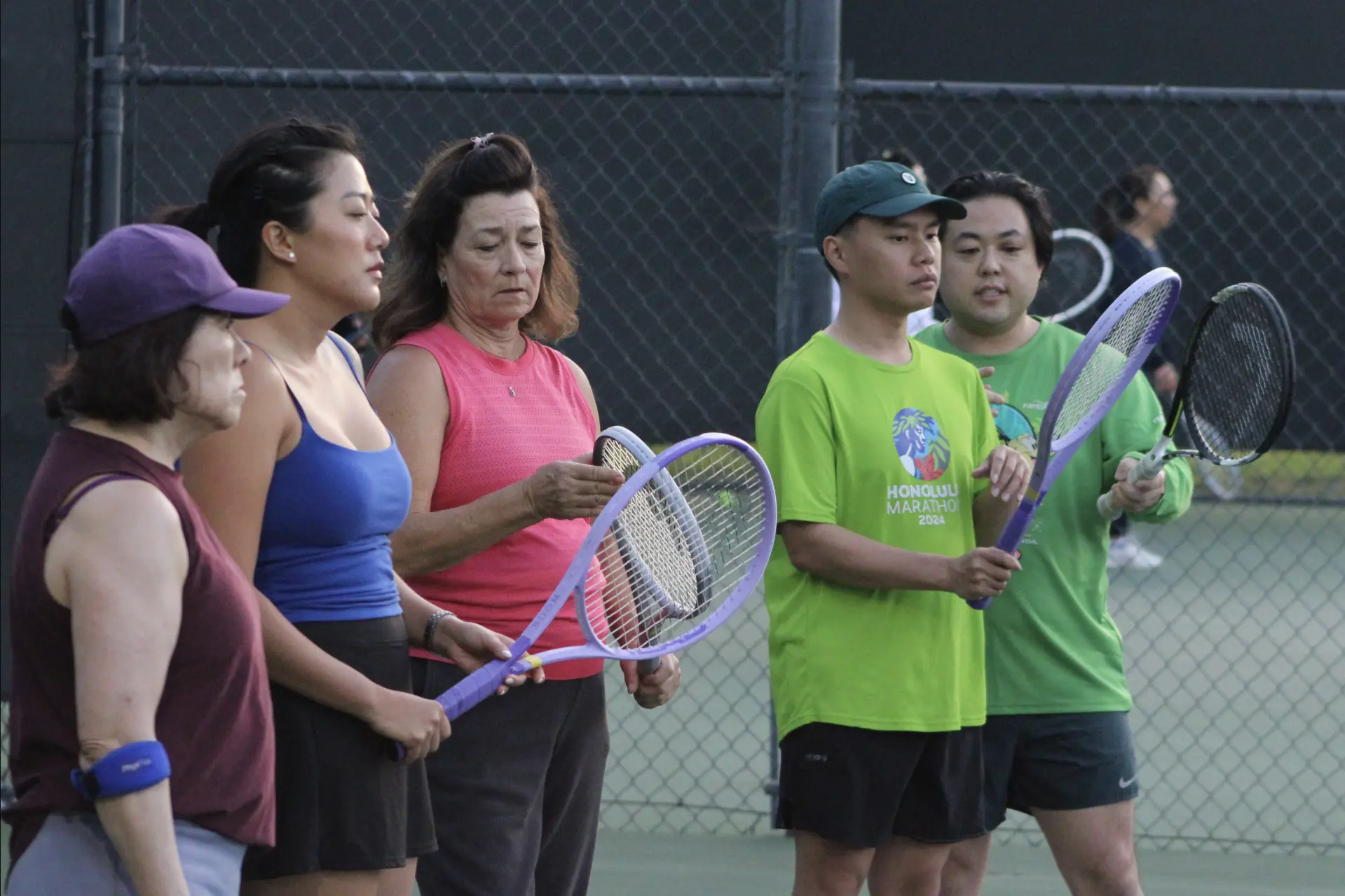Group of adults holding tennis rackets on court
