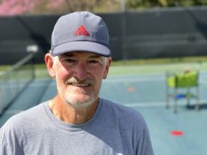 Jim F in a Baseball Cap in Front of a Tennis Ground