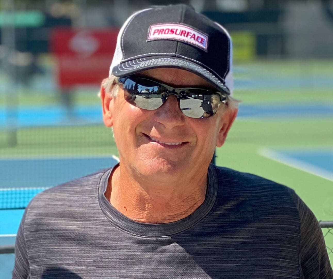 Man wearing sunglasses and cap on tennis court.