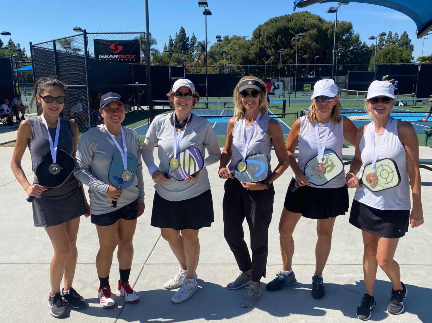 Six women holding pickleball paddles, wearing medals.